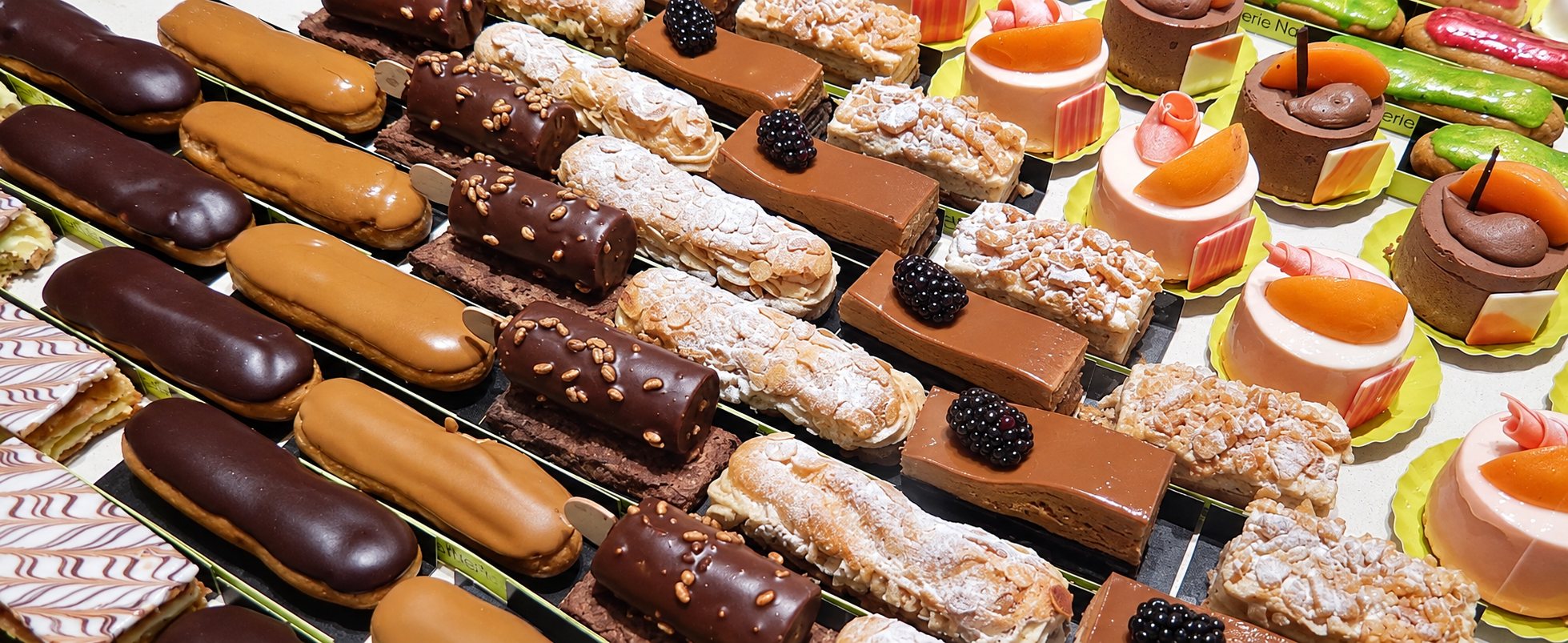 Vitrine de pâtisserie présentant des rangées d'éclairs au chocolat et au caramel, de gâteaux aux mûres, de millefeuilles et d'entremets à l'abricot.