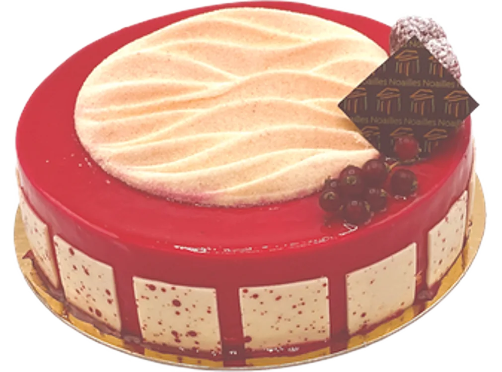 Un entremets rond au glaçage rouge brillant, orné d'un disque beige ondulé, de fruits rouges et d'une plaquette en chocolat, posé sur un carton doré.