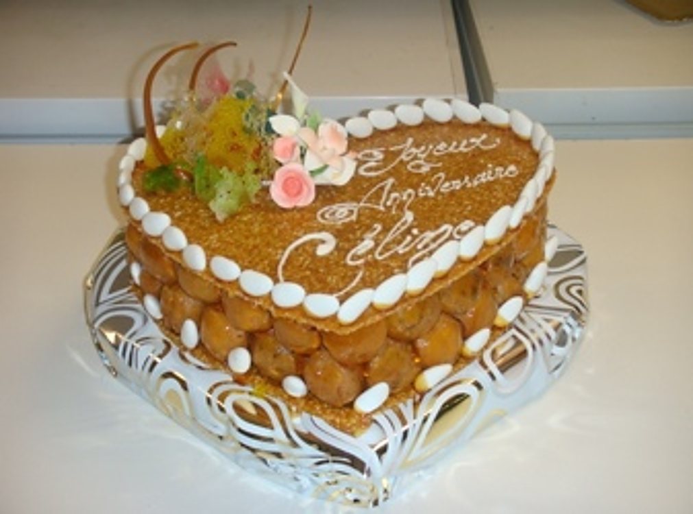 Un gâteau en forme de cœur garni de petits choux caramélisés et de fleurs en sucre, avec un message d'anniversaire écrit sur le dessus.