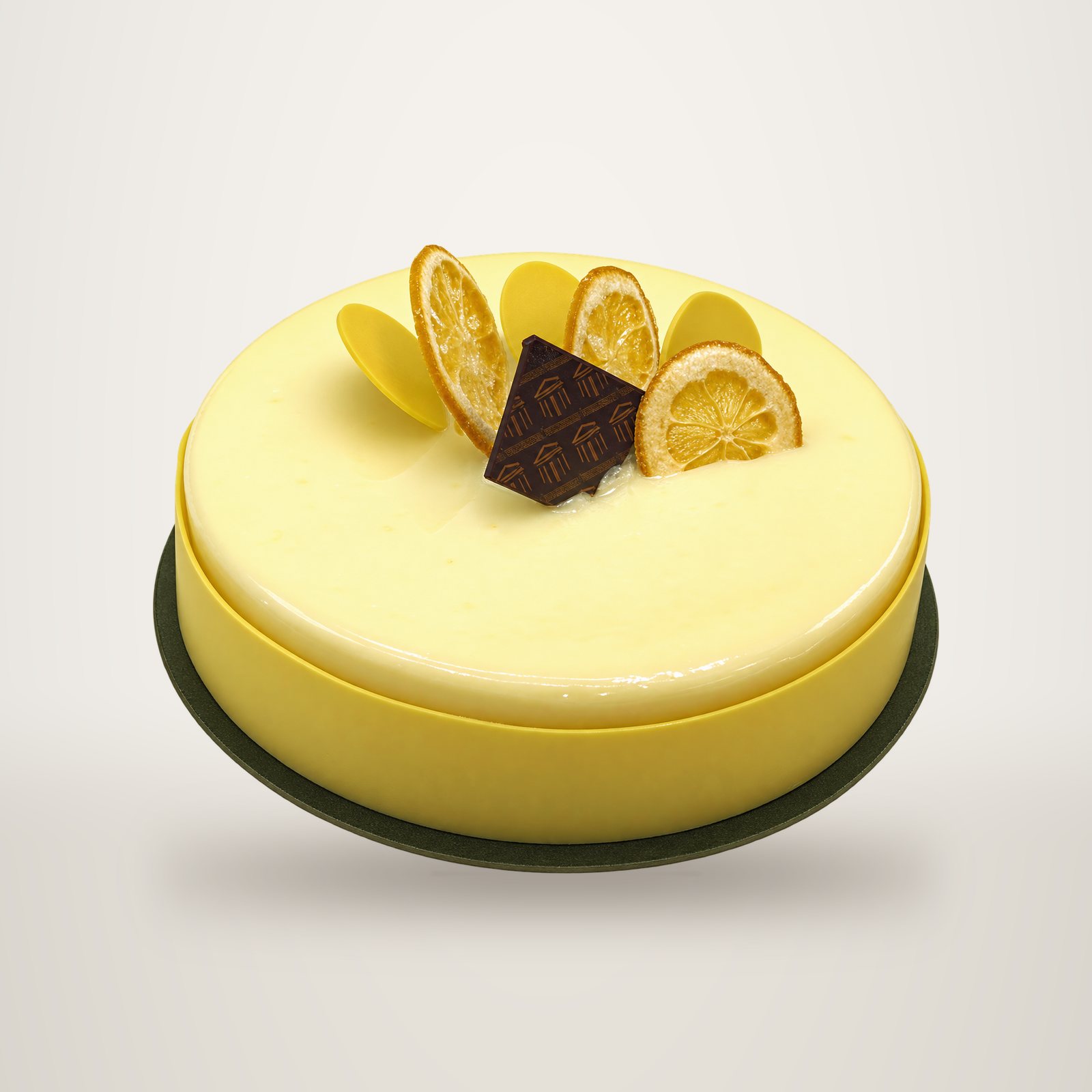 Un gâteau rond au citron recouvert d'une crème jaune pâle, décoré de tranches de citron confites et d'un carré de chocolat noir, posé sur un disque noir.