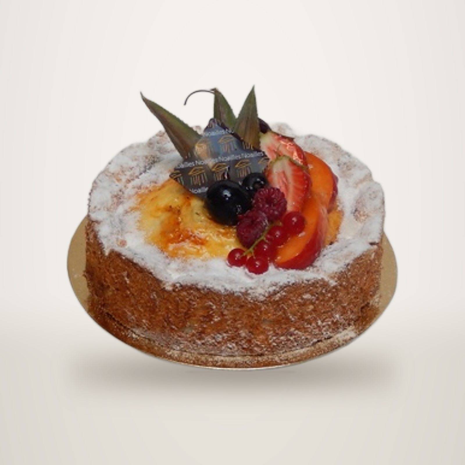 Un gâteau rond aux côtés couverts de croustillant, décoré de fruits frais, raisins, framboises, groseilles et tranches de pêche, posé sur un carton doré.