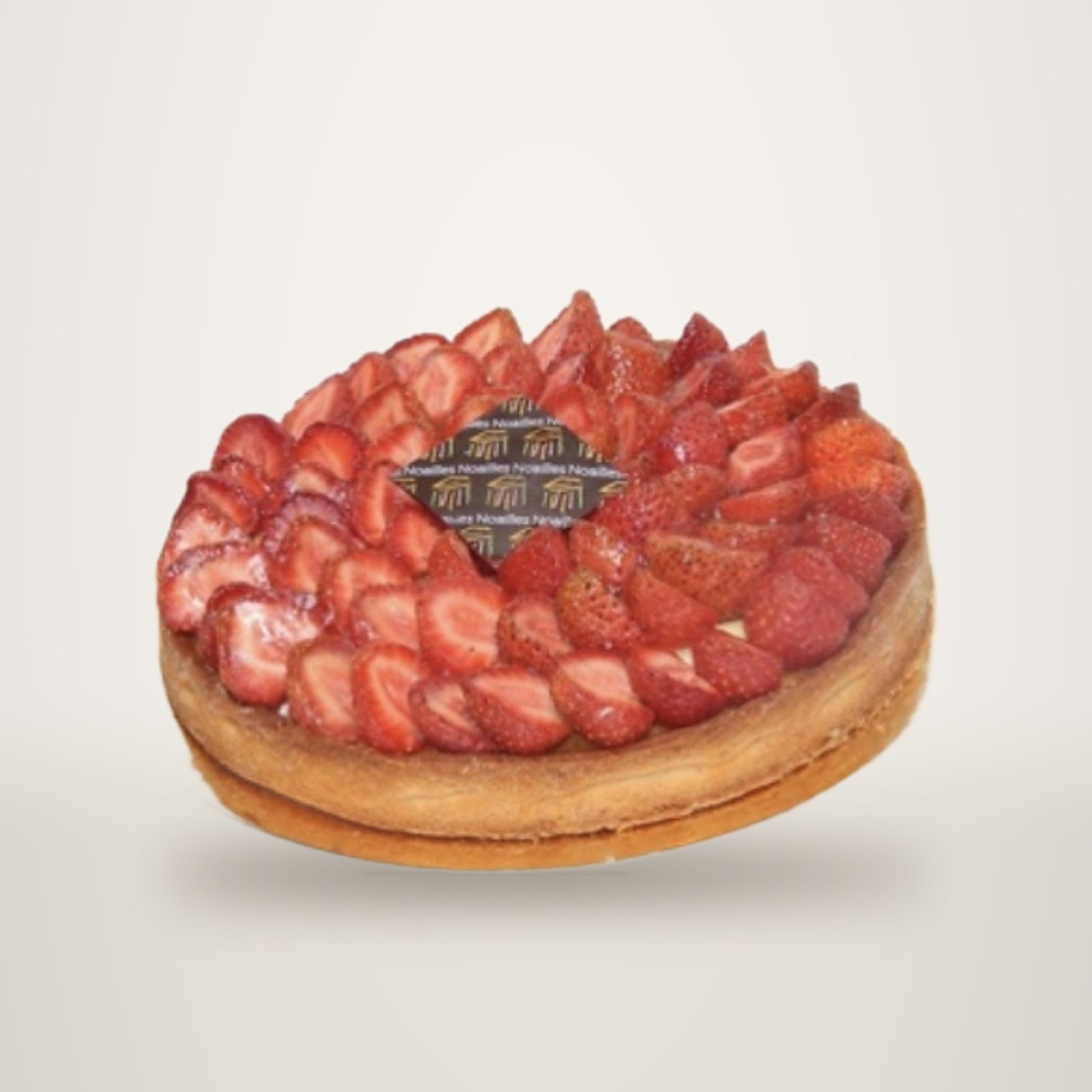 Une tarte ronde garnie de tranches de fraises fraîches disposées en cercle autour d'une plaque en chocolat décorée, posée sur un plateau doré.